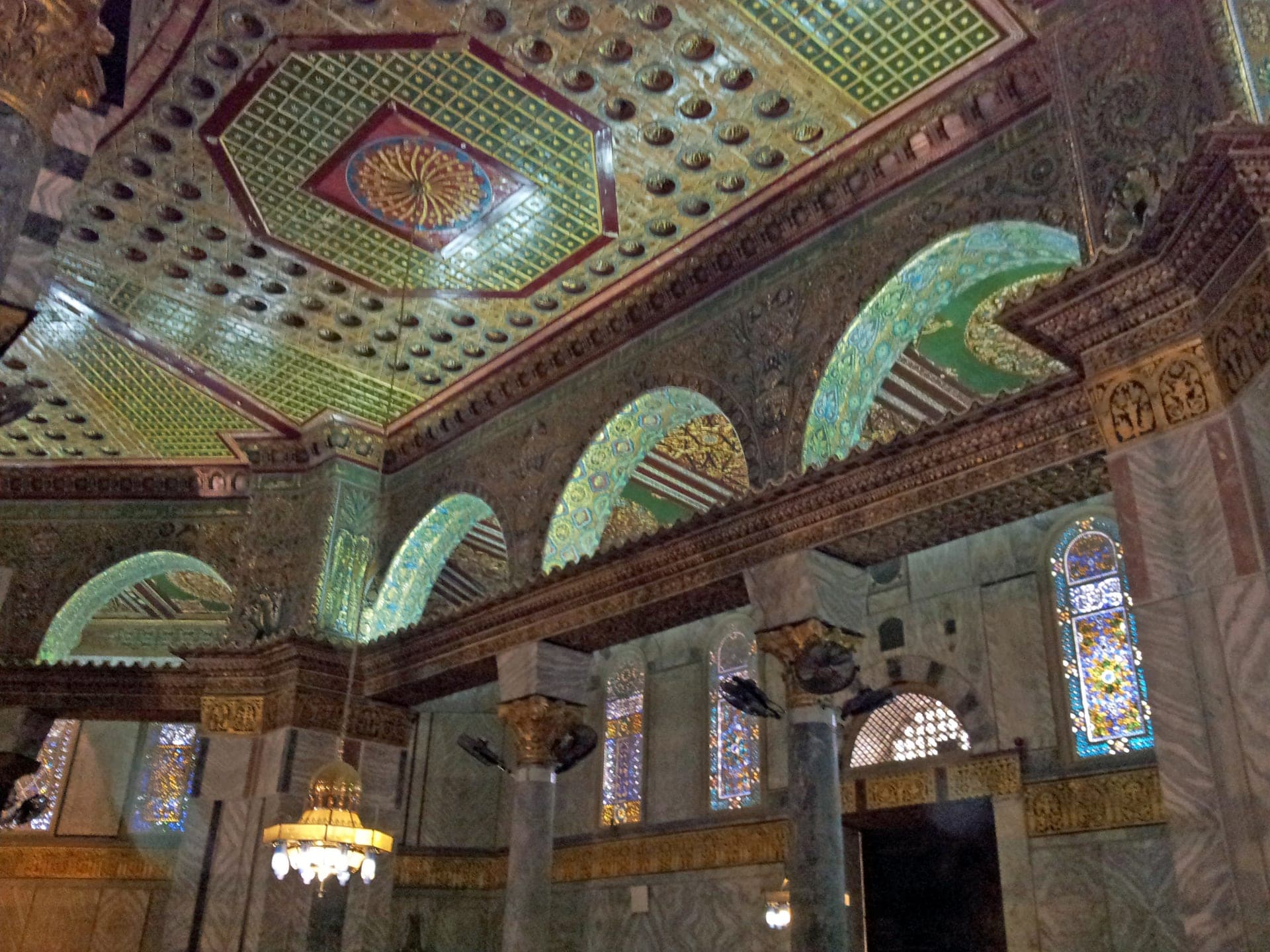 Interior mosaics and arcade of the Dome of the Rock in gold, green, and blue glass tesserae, where the inscription band runs